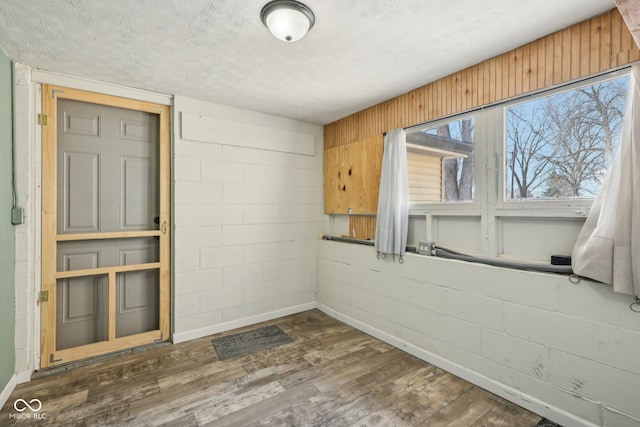 unfurnished room with dark wood finished floors, a textured ceiling, concrete block wall, and baseboards