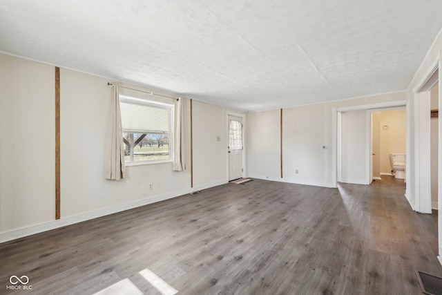 unfurnished living room featuring visible vents, baseboards, and wood finished floors