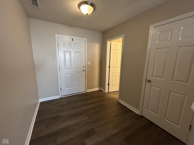 hallway featuring visible vents, baseboards, a textured ceiling, and dark wood-style floors