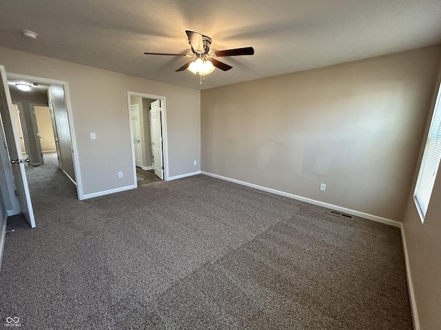 unfurnished bedroom featuring visible vents, connected bathroom, dark colored carpet, baseboards, and ceiling fan