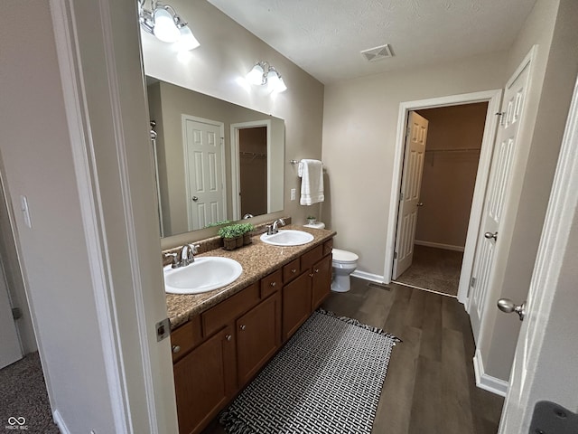 bathroom featuring toilet, wood finished floors, visible vents, and a sink