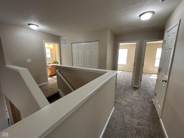 hallway featuring dark colored carpet, visible vents, an upstairs landing, and baseboards