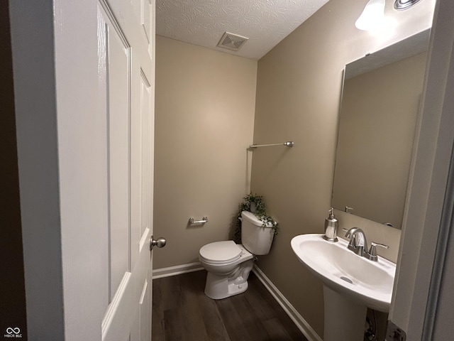 half bathroom with wood finished floors, baseboards, visible vents, a textured ceiling, and toilet