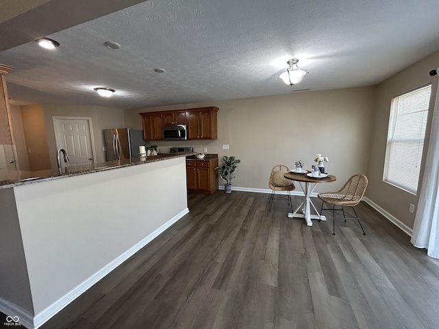 kitchen featuring dark wood-type flooring, baseboards, dark stone counters, appliances with stainless steel finishes, and a textured ceiling