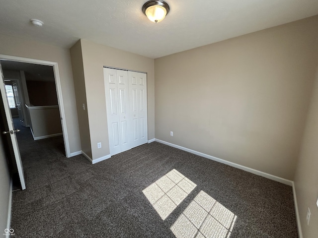 unfurnished bedroom featuring dark carpet, baseboards, and a closet