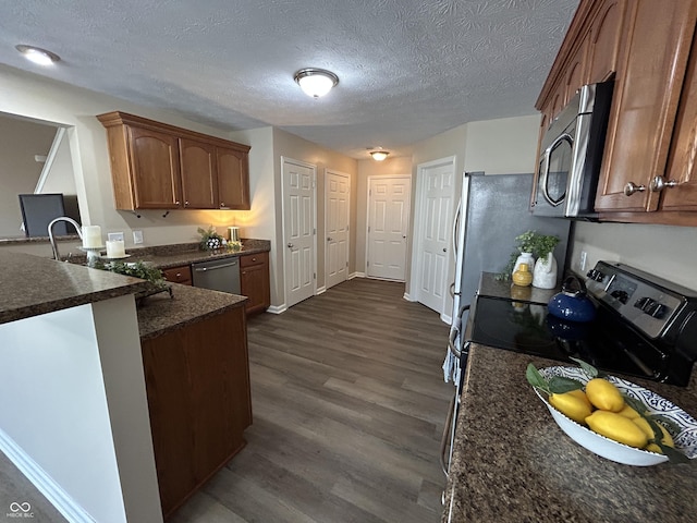 kitchen featuring dark wood-style flooring, a peninsula, a textured ceiling, stainless steel appliances, and a sink