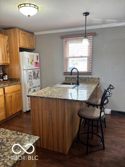 kitchen with crown molding, dark wood finished floors, a breakfast bar area, freestanding refrigerator, and a sink