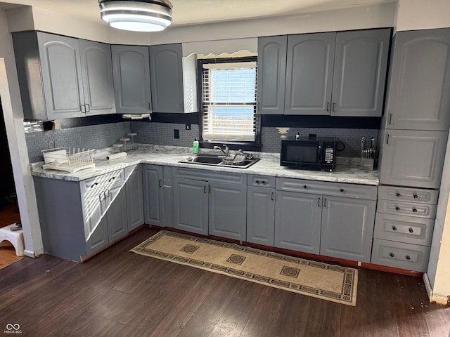 kitchen with dark wood-style floors, gray cabinets, a sink, black microwave, and backsplash