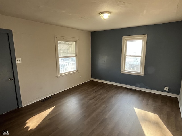 spare room with dark wood-style floors, visible vents, and a healthy amount of sunlight