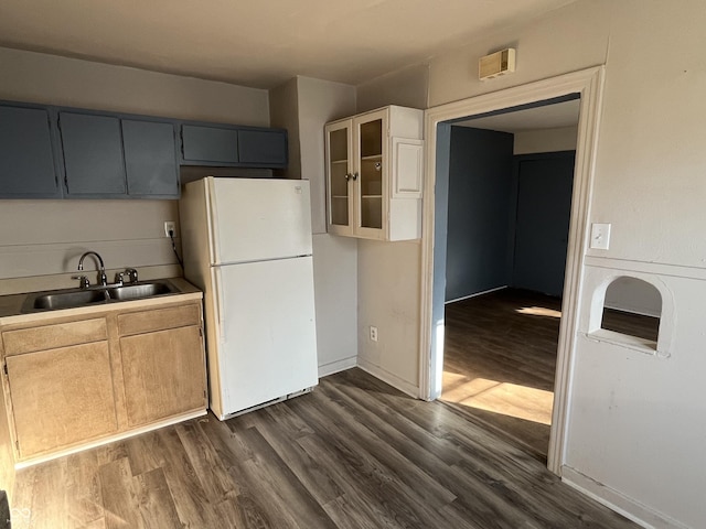 kitchen with a sink, gray cabinetry, glass insert cabinets, freestanding refrigerator, and dark wood-style flooring