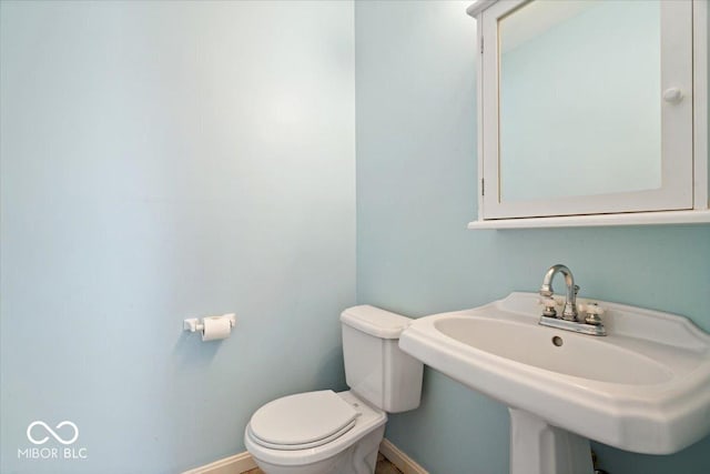 half bath with a sink, baseboards, and toilet