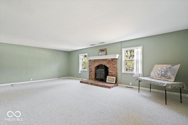 unfurnished living room with a wealth of natural light, baseboards, carpet floors, and a wood stove