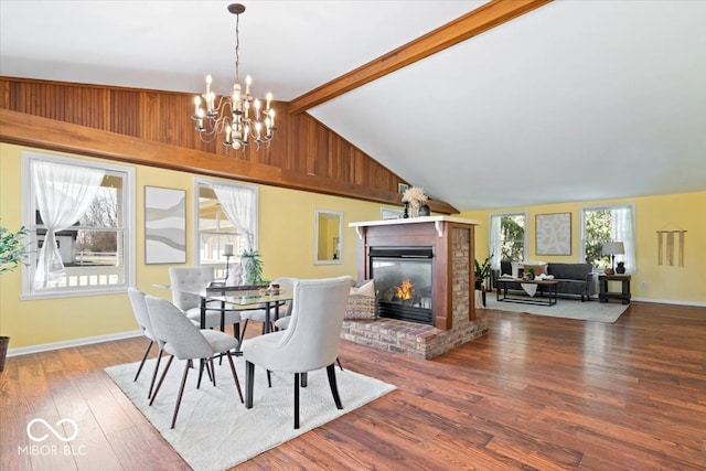 dining space with beam ceiling, a glass covered fireplace, wood finished floors, an inviting chandelier, and baseboards