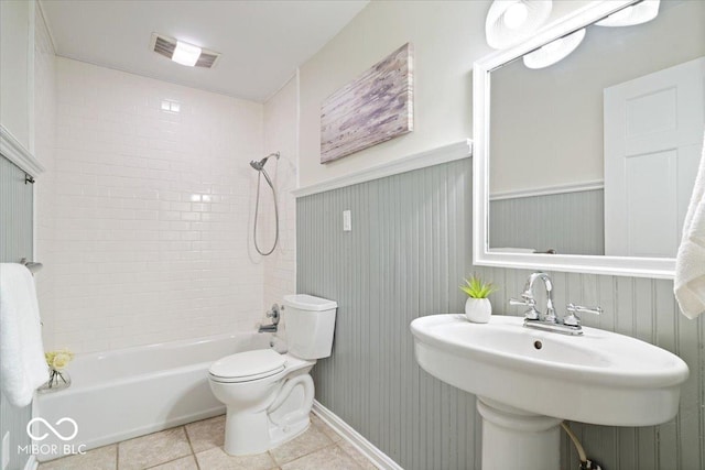 full bath featuring toilet, shower / tub combination, wainscoting, tile patterned floors, and a sink