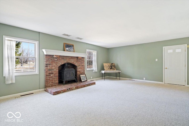 unfurnished living room with a wood stove, carpet flooring, baseboards, and visible vents