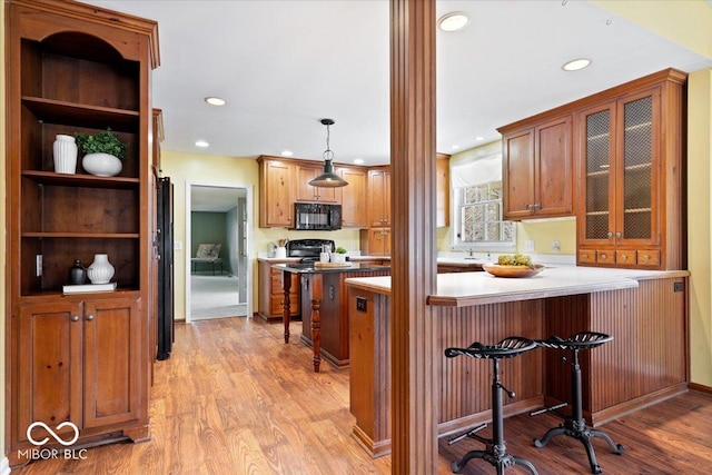 kitchen with light wood-style floors, a peninsula, a breakfast bar area, and black microwave