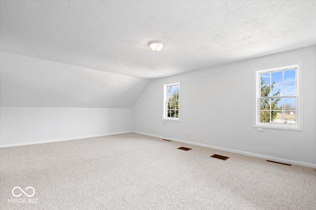 additional living space with vaulted ceiling, visible vents, a textured ceiling, and carpet floors