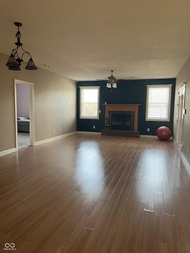 unfurnished living room featuring baseboards, a textured ceiling, a brick fireplace, and dark wood-style flooring