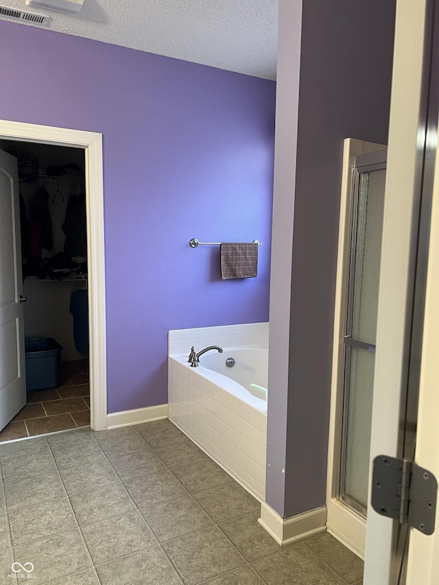 bathroom with visible vents, a shower stall, a walk in closet, a garden tub, and a textured ceiling