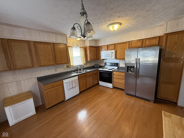 kitchen with a sink, white appliances, dark countertops, and brown cabinets