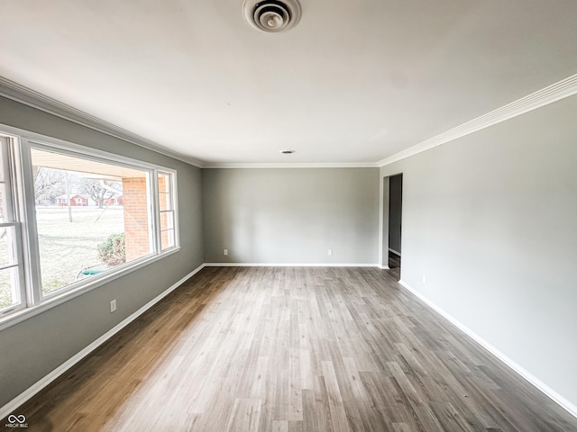 empty room with crown molding, wood finished floors, baseboards, and visible vents