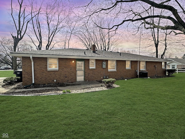 back of property at dusk with brick siding, a lawn, a chimney, and central AC