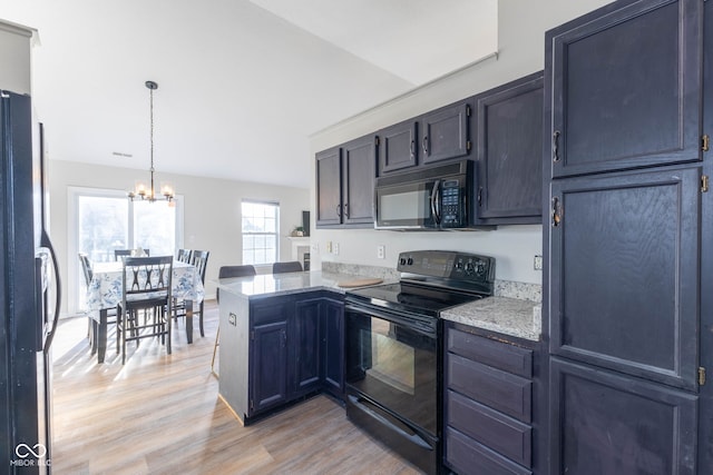 kitchen with light wood finished floors, an inviting chandelier, a peninsula, black appliances, and pendant lighting