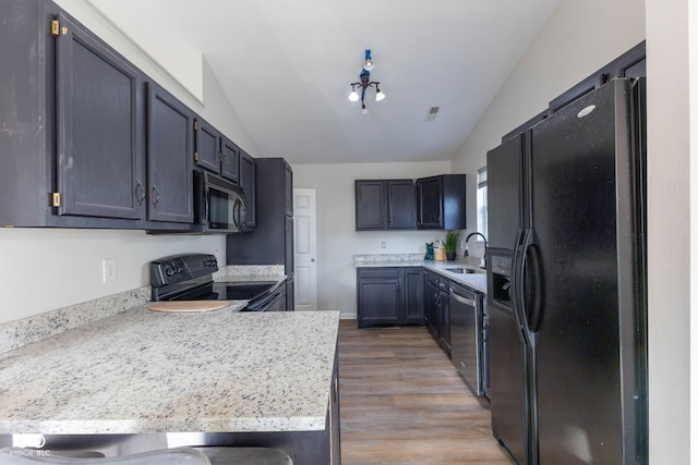 kitchen featuring black appliances, vaulted ceiling, a peninsula, and a sink