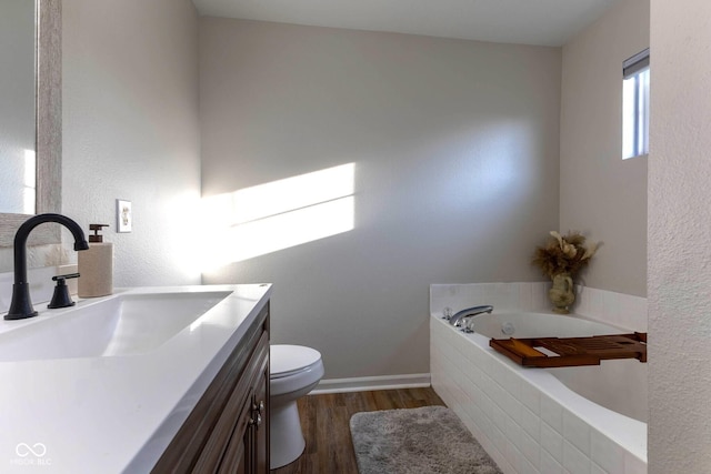 bathroom with baseboards, toilet, a garden tub, wood finished floors, and vanity