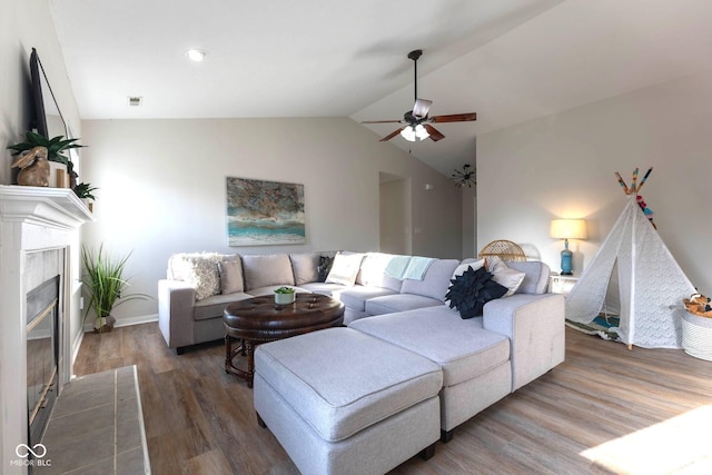 living area featuring visible vents, a tiled fireplace, wood finished floors, ceiling fan, and vaulted ceiling