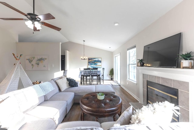 living area featuring a tiled fireplace, ceiling fan with notable chandelier, wood finished floors, and vaulted ceiling