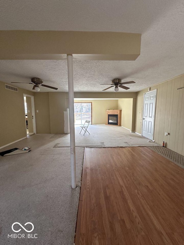 unfurnished living room featuring visible vents, a ceiling fan, a textured ceiling, wood finished floors, and a glass covered fireplace