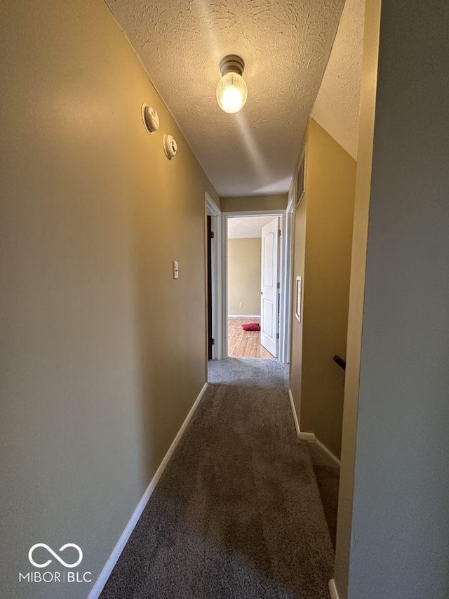 hall featuring visible vents, baseboards, a textured ceiling, and carpet flooring