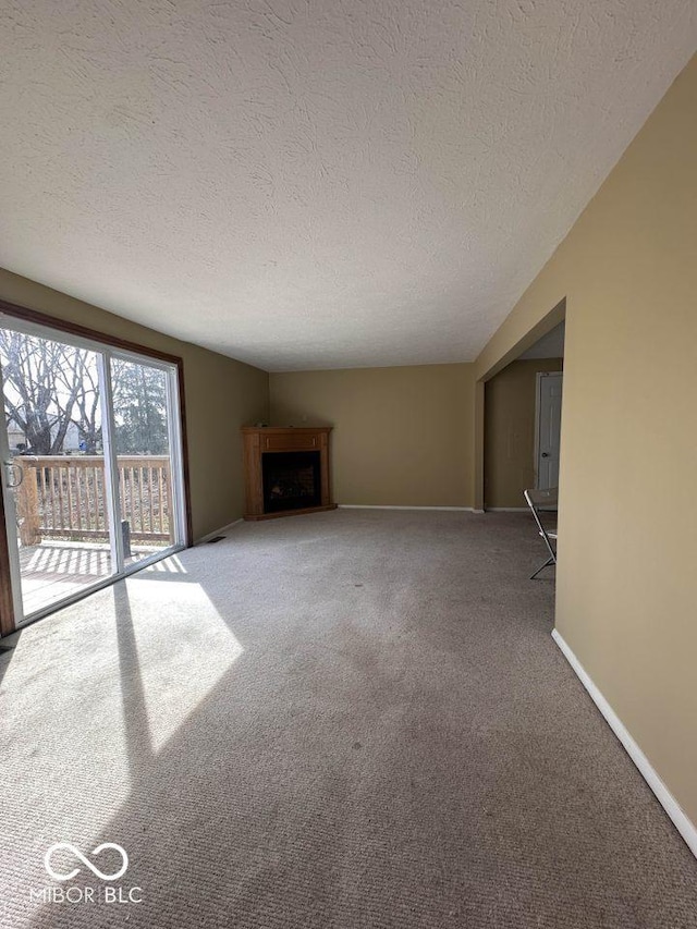 unfurnished living room with a textured ceiling, a fireplace, baseboards, and carpet