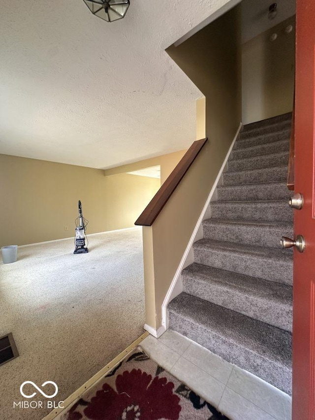 staircase with carpet, baseboards, and a textured ceiling