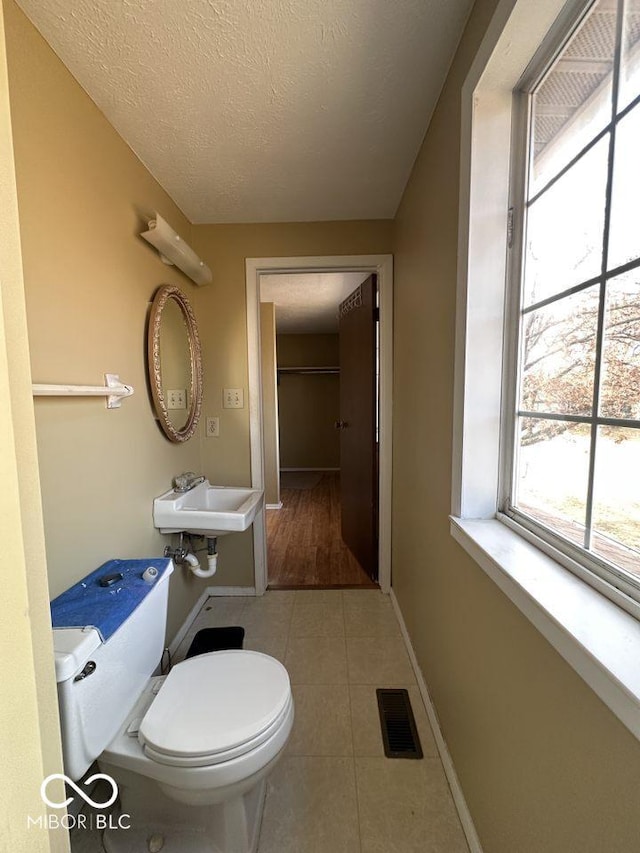 half bathroom featuring visible vents, toilet, tile patterned floors, a textured ceiling, and a sink