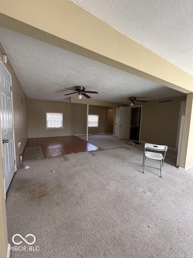 unfurnished living room featuring visible vents, carpet, ceiling fan, and a textured ceiling