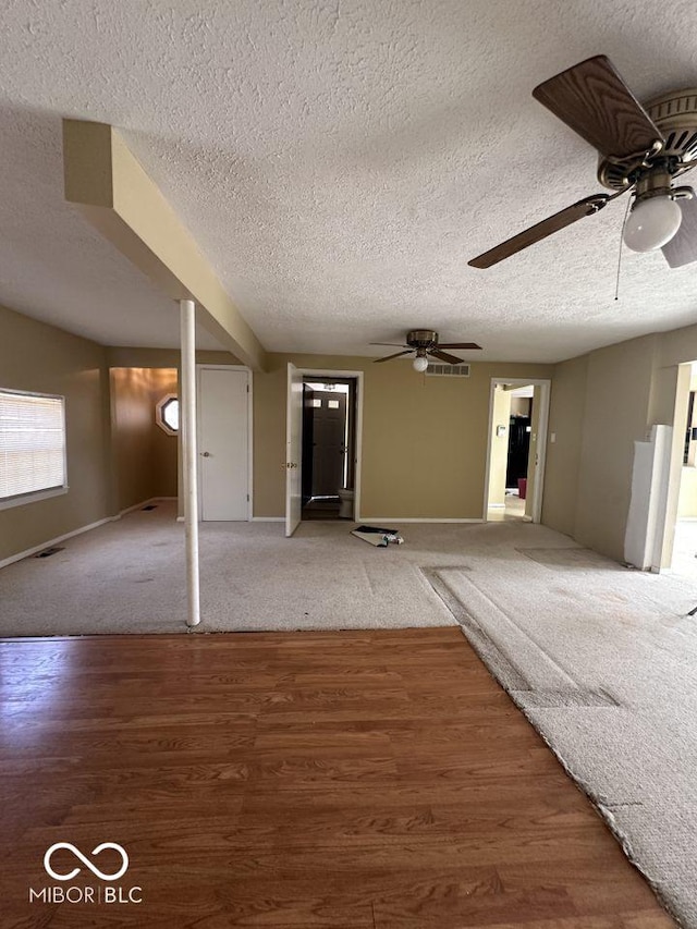 unfurnished living room featuring a textured ceiling, wood finished floors, visible vents, and ceiling fan