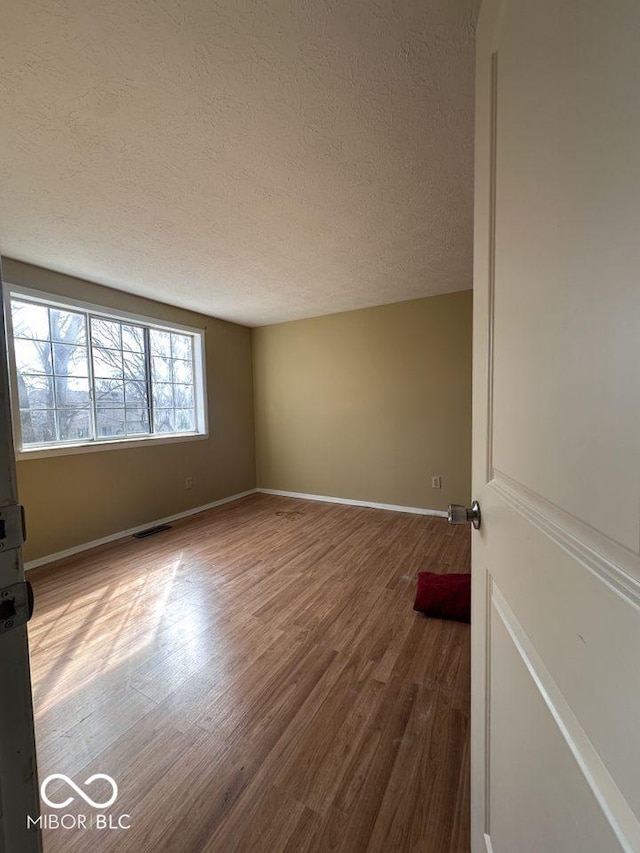 unfurnished room with visible vents, a textured ceiling, baseboards, and wood finished floors