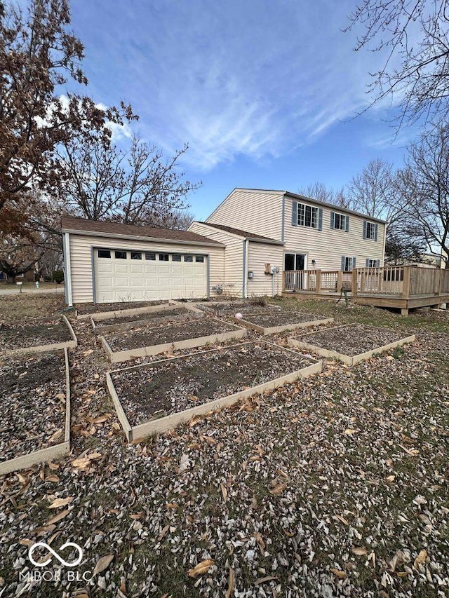 exterior space featuring a vegetable garden, a garage, driveway, and a wooden deck