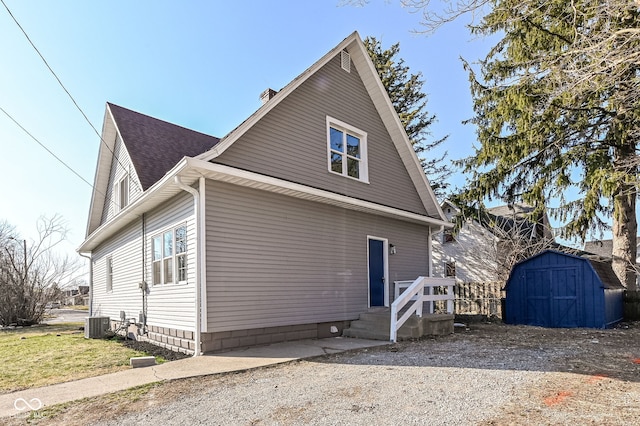 view of side of home featuring a storage shed, central AC unit, an outbuilding, and a shingled roof