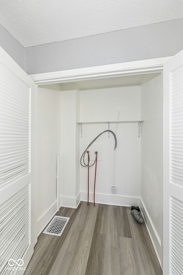 laundry area featuring hookup for a washing machine, wood finished floors, visible vents, baseboards, and a textured ceiling