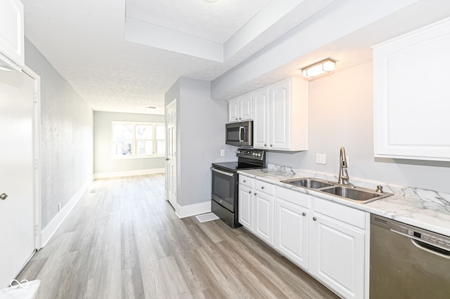 kitchen featuring appliances with stainless steel finishes, light wood-style floors, white cabinets, a textured ceiling, and a sink