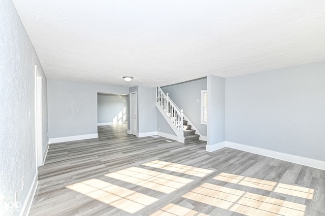 unfurnished room with stairway, baseboards, a textured ceiling, and wood finished floors