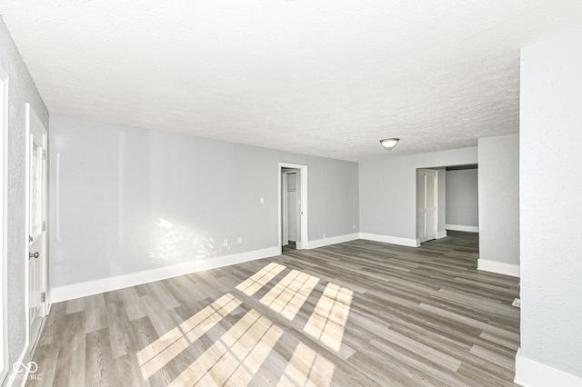 spare room featuring a textured ceiling, baseboards, and wood finished floors