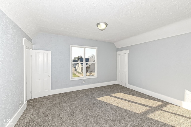 empty room with vaulted ceiling, carpet, a textured wall, and a textured ceiling