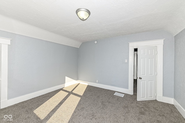 carpeted empty room featuring vaulted ceiling, a textured wall, baseboards, and a textured ceiling