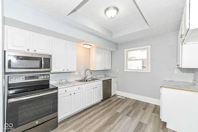 kitchen with light wood-type flooring, a sink, a tray ceiling, white cabinetry, and appliances with stainless steel finishes