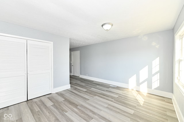 unfurnished bedroom with visible vents, a textured ceiling, a closet, light wood-style floors, and baseboards