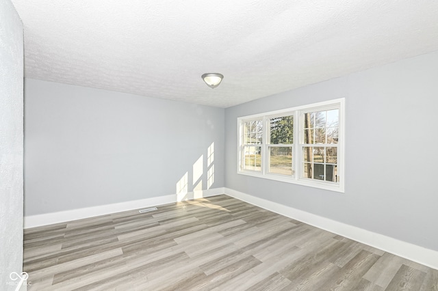 empty room featuring a textured ceiling, baseboards, and wood finished floors